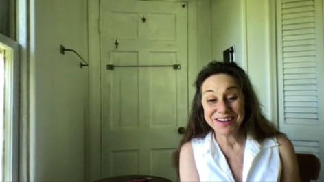 Amy wearing a white top and smiling at the camera while sitting in front of a door