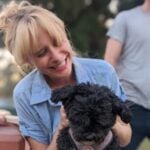 Julia smiling while looking and holding a black dog