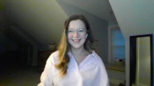 Laura is a woman with long fair hair and wearing glasses and a white shirt while in a room, smiling at the camera, talking about her insomnia transformation.