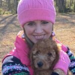 Anne smiling while wearing a pink hat and holding a dog