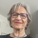 Therese has short gray hair and is wearing glasses as she smiles at the camera.