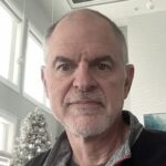 Daniel is indoors with large windows in the background. He is facing the camera.