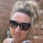 Heather has tall fair hair and is wearing sunglasses while smiling at the camera.