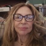 Kathy has long, fair hair and is wearing glasses and smiling at the camera