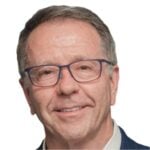 Stephen has short, fair hair, is wearing glasses, and smiling at the camera against a while background.