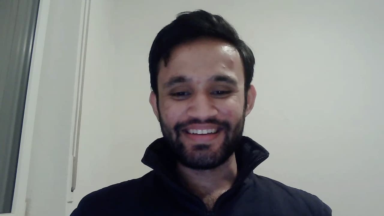 Farrukh is a man with dark hair and a beard. He is looking at the camera and smiling.