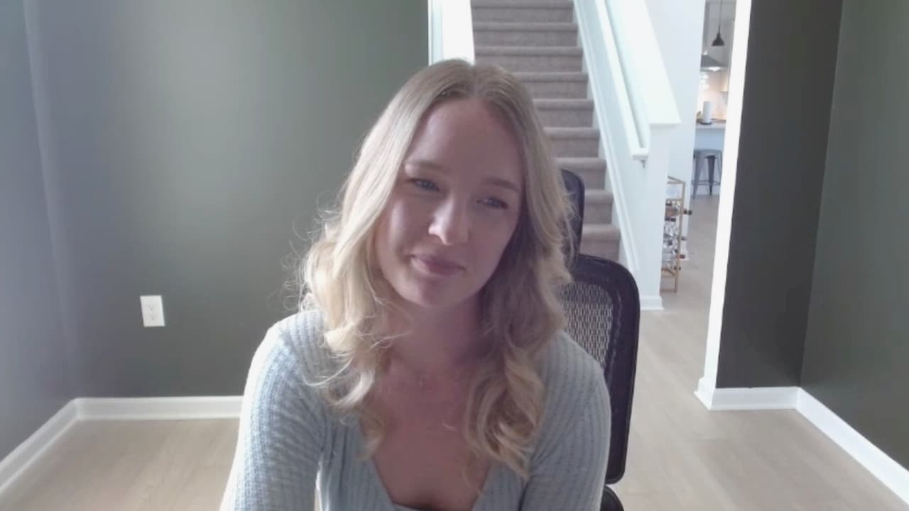 Woman sitting in a chair during a video call in a bright home office with a staircase in the background.