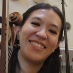 Smiling woman seated beside a violin in an indoor music setting.