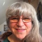 Close-up portrait of a smiling woman with gray hair and glasses.